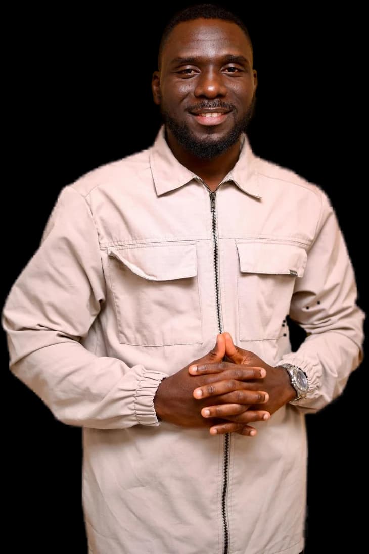 Oyewale Abdullah Muftau smiling, hands clasped, wearing a stone-coloured jacket